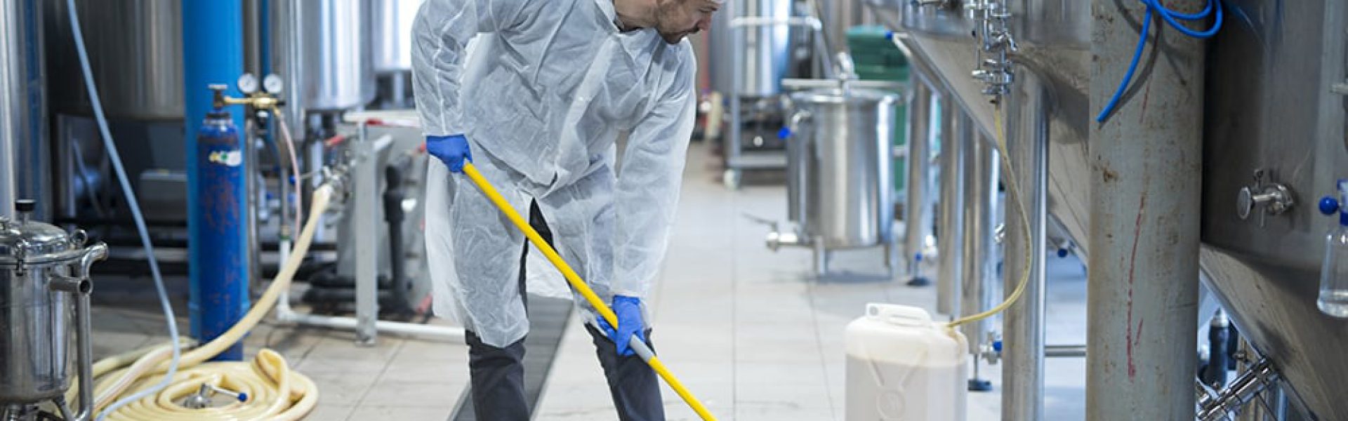 Professional industrial cleaner in protective uniform cleaning floor of food processing plant.