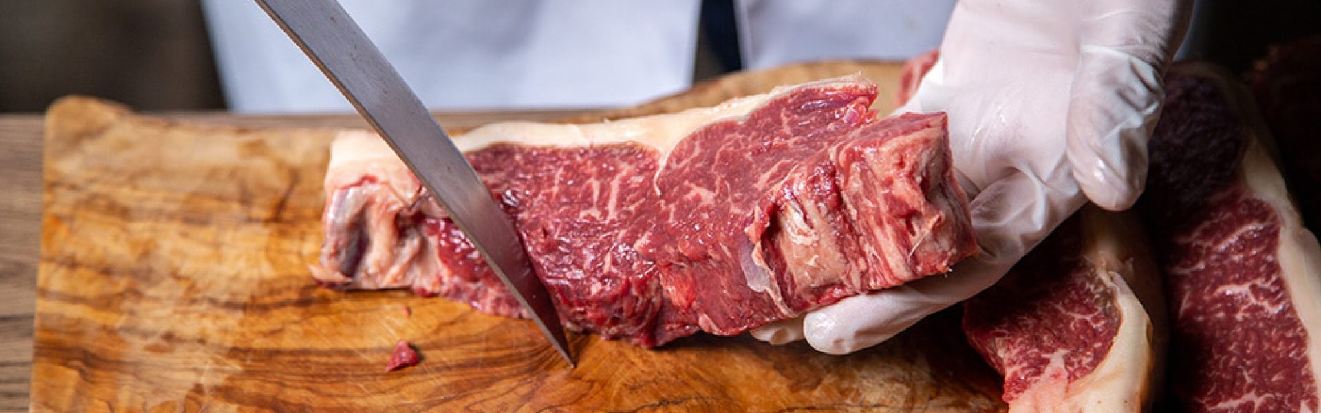 front view butcher cutting meat in white gloves holding big knife on the wooden desk meat job butcher kitchen